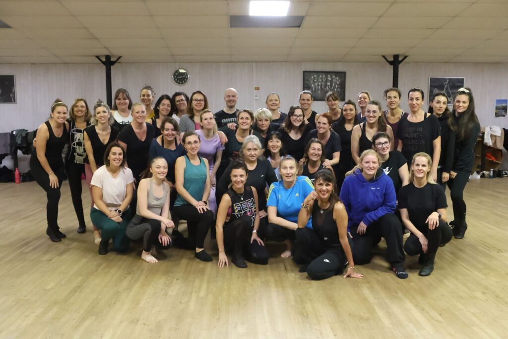 Groupe d’adultes de tous âges réunis dans un studio de danse, posant et souriant après un cours, sur un sol en bois clair.