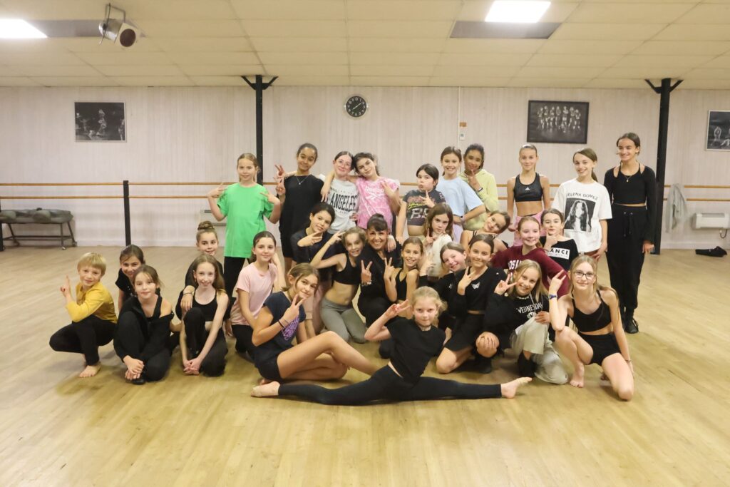 Groupe d’enfants et adolescents posant dans un studio de danse, souriants, habillés en tenue de danse, sur un parquet de salle avec miroirs en fond